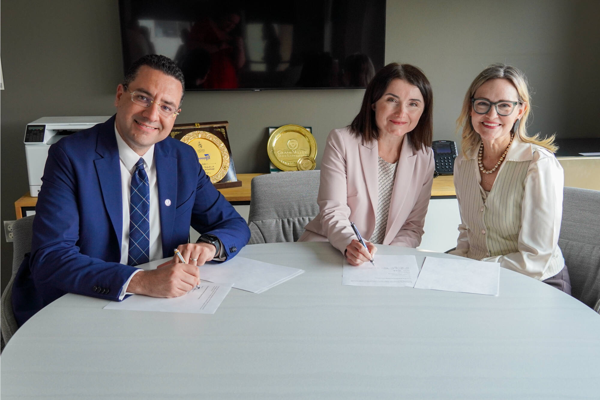 Marouane Kessentini, dean of GVSU’s College of Computing; Yuhila Alhatou, co-founder of The Mitten Project; and Jennifer Wangler, vice president of technology at The Right Place, smile while signing a Memorandum of Understanding.